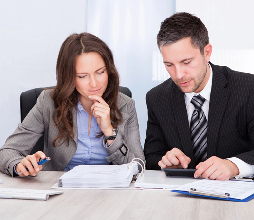 Two Young Business people Calculating Bills At Desk In Office